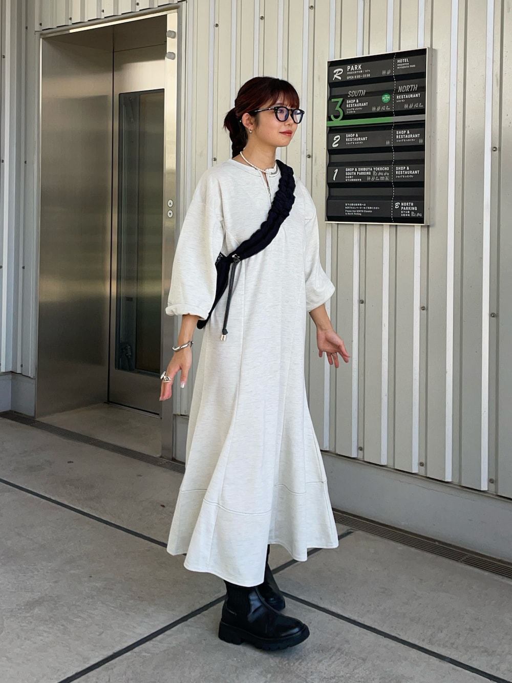 グレー系のワンピース、ブラック系のブーツ、ブラック系のショルダーバッグを着用したレディースの秋コーディネートの1枚目の写真