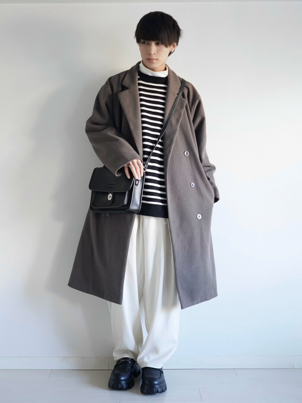 ベージュ系のチェスターコート、ブラック系のニット/セーター、ホワイト系のTシャツ/カットソーを着用したメンズの冬コーディネートの1枚目の写真