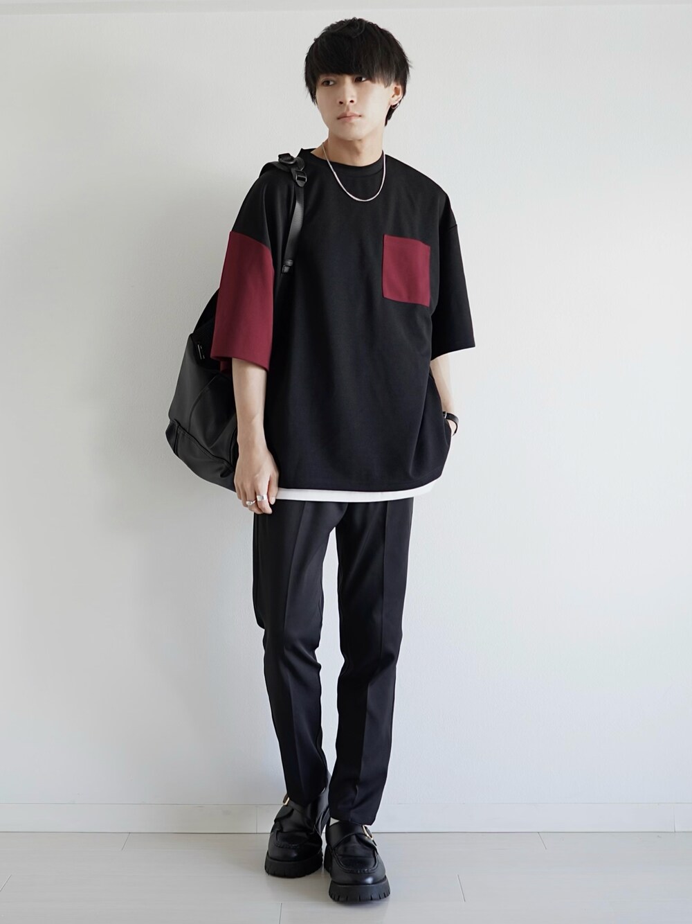 レッド系のTシャツ/カットソー、ブラック系のスラックス、ブラック系のバックパック/リュックを着用したメンズの夏コーディネートの1枚目の写真