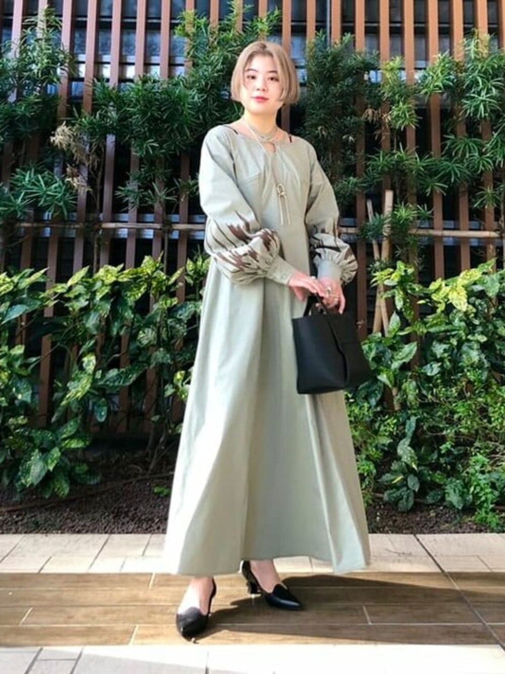 グリーン系のワンピース、ブラック系のトートバッグ、ブラック系のパンプスを着用したレディースの冬コーディネートの1枚目の写真