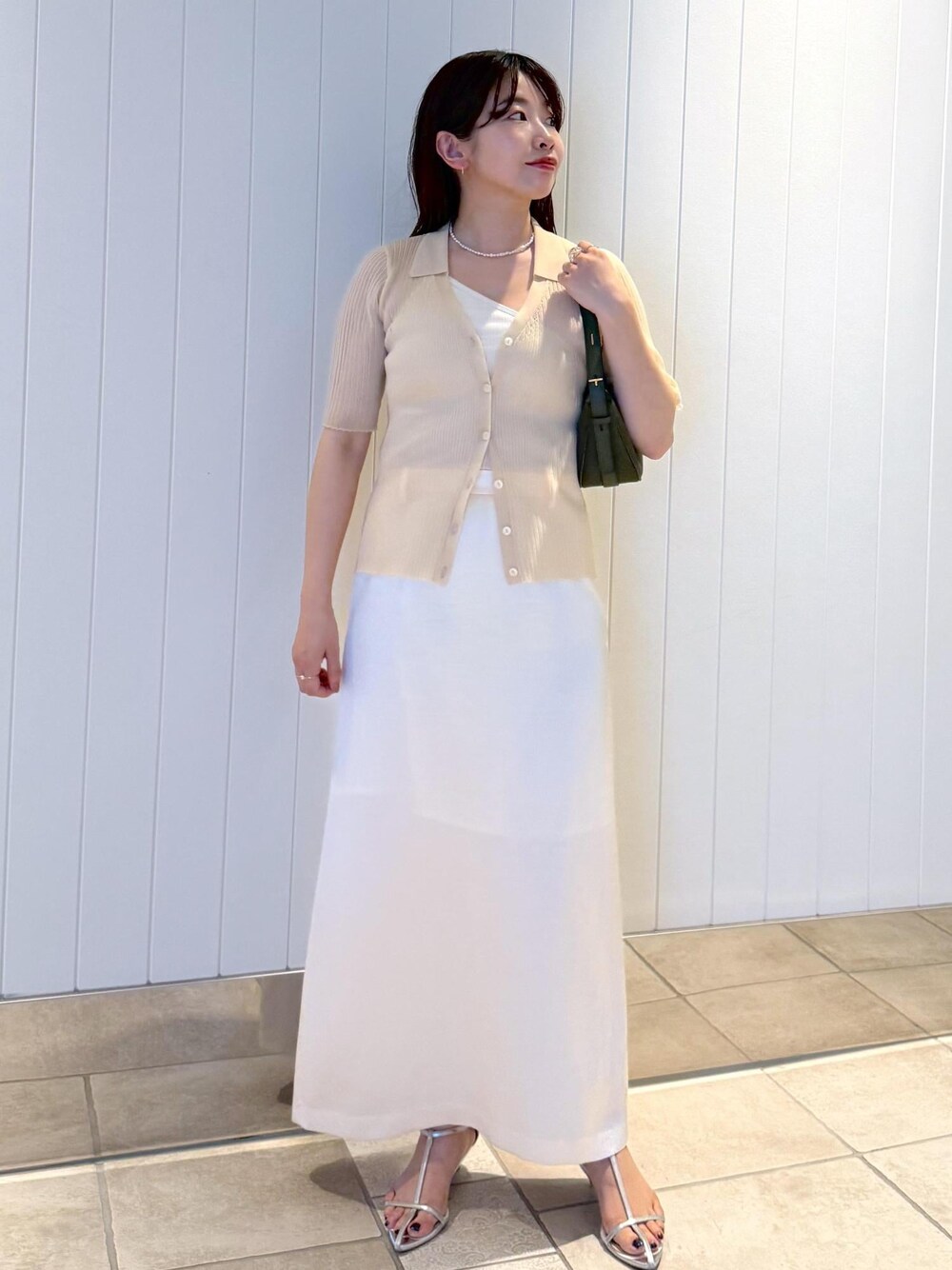 ホワイト系のスカート、ベージュ系のニット/セーター、グリーン系のハンドバッグを着用したレディースの夏コーディネートの1枚目の写真