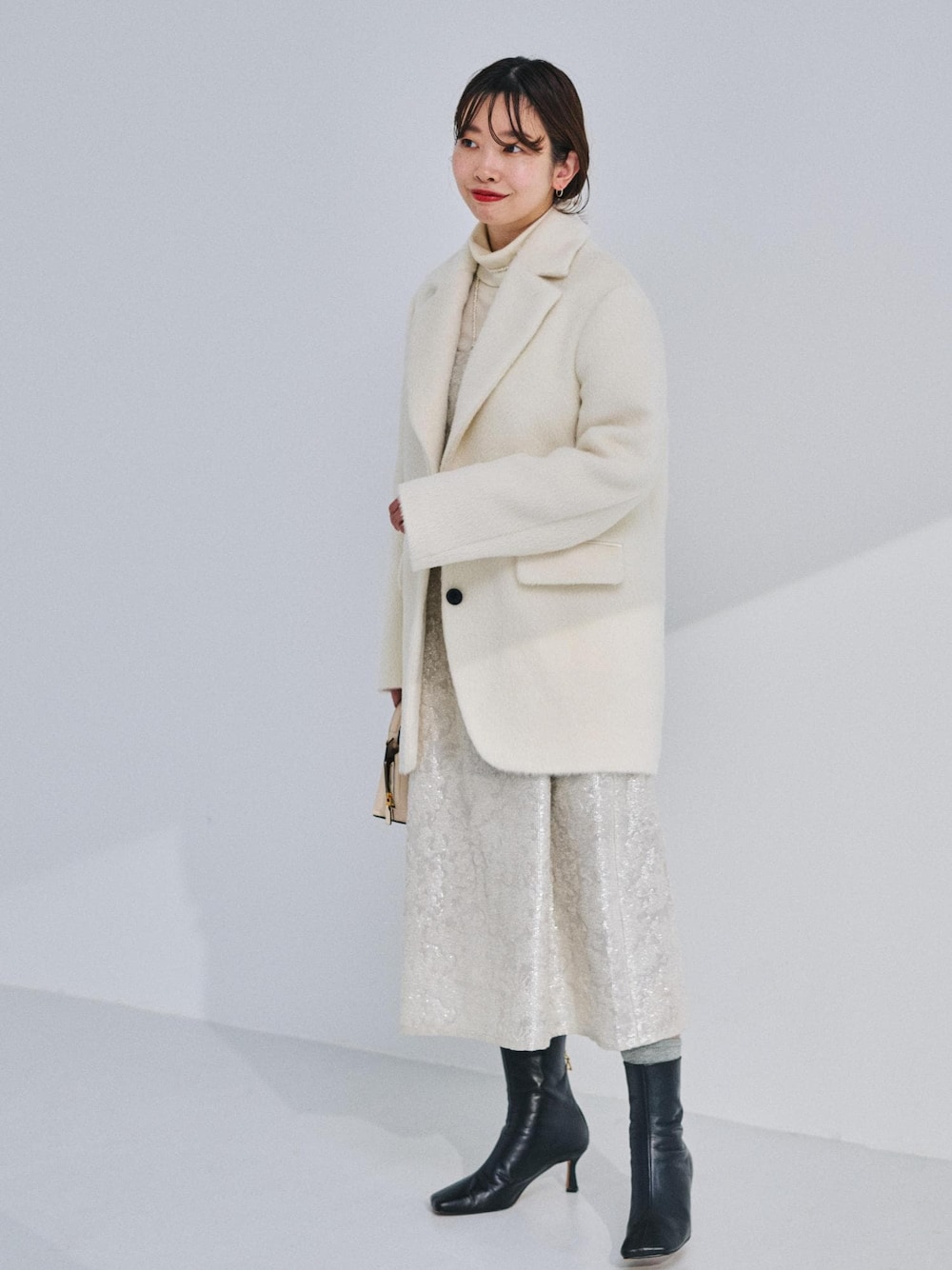 ベージュ系のショルダーバッグ、ブラック系のブーツ、ホワイト系のテーラードジャケットを着用したレディースの冬コーディネートの1枚目の写真