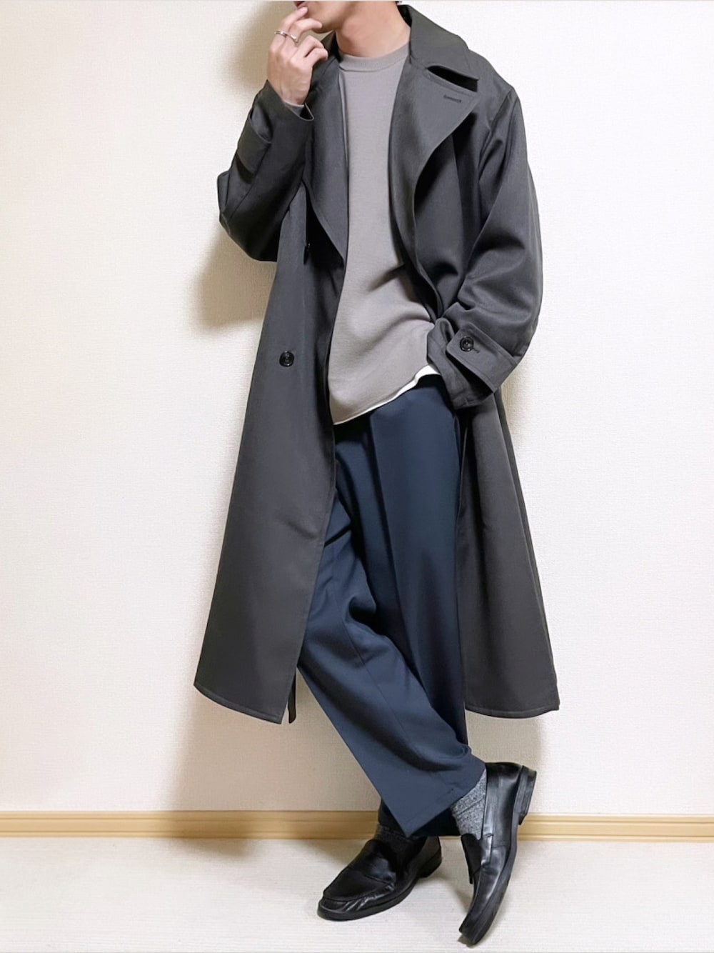 グレー系のトレンチコート、ベージュ系のニット/セーター、ホワイト系のタンクトップを着用したメンズの秋コーディネートの1枚目の写真