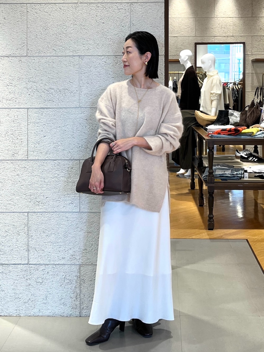 ホワイト系のスカート、ベージュ系のニット/セーター、ブラウン系のブーツを着用したレディースの秋コーディネートの1枚目の写真