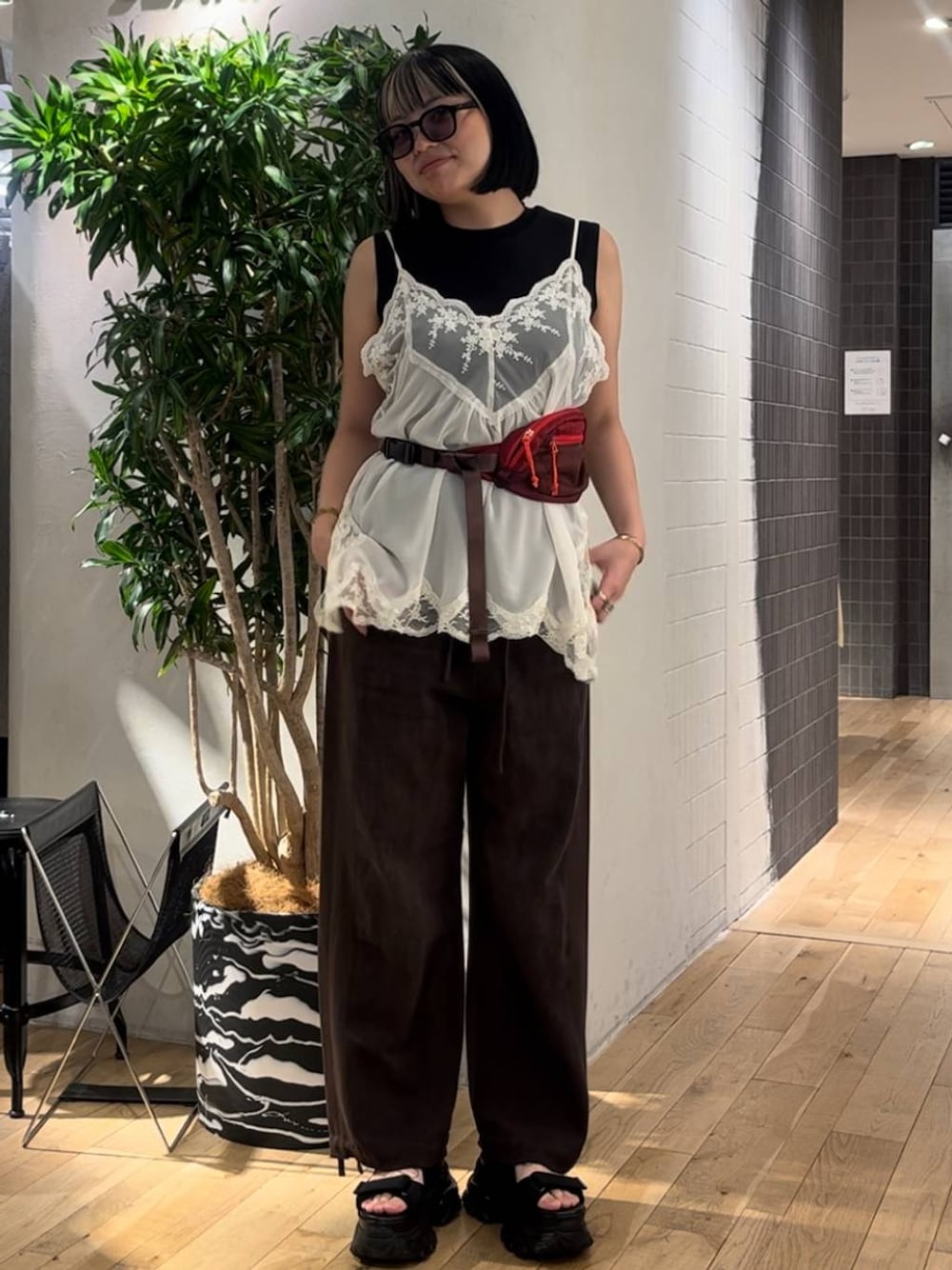ホワイト系のキャミソール、ブラウン系のデニムパンツ、ブラック系のサンダルを着用したレディースの夏コーディネートの1枚目の写真