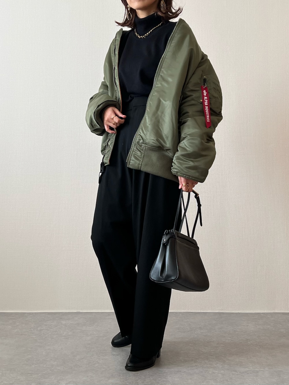 グリーン系のMA-1、ブラック系のニット/セーター、ブラック系のスラックスを着用したレディースの冬コーディネートの1枚目の写真