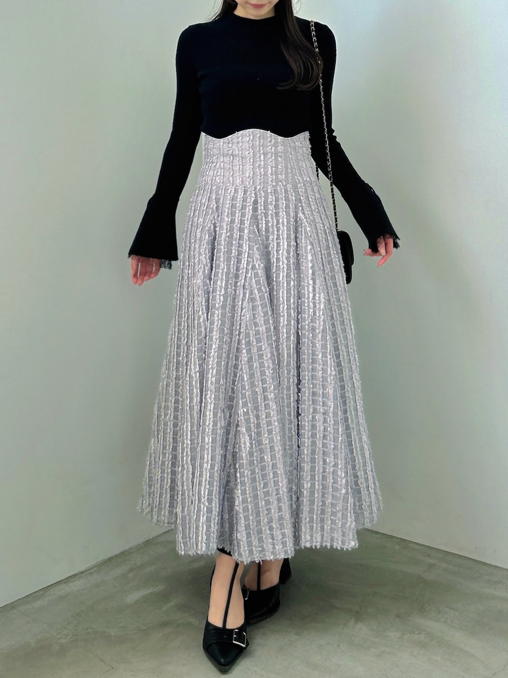 ブラック系のニット/セーター、グレー系のスカート、ブラック系のパンプスを着用したレディースの秋コーディネートの1枚目の写真