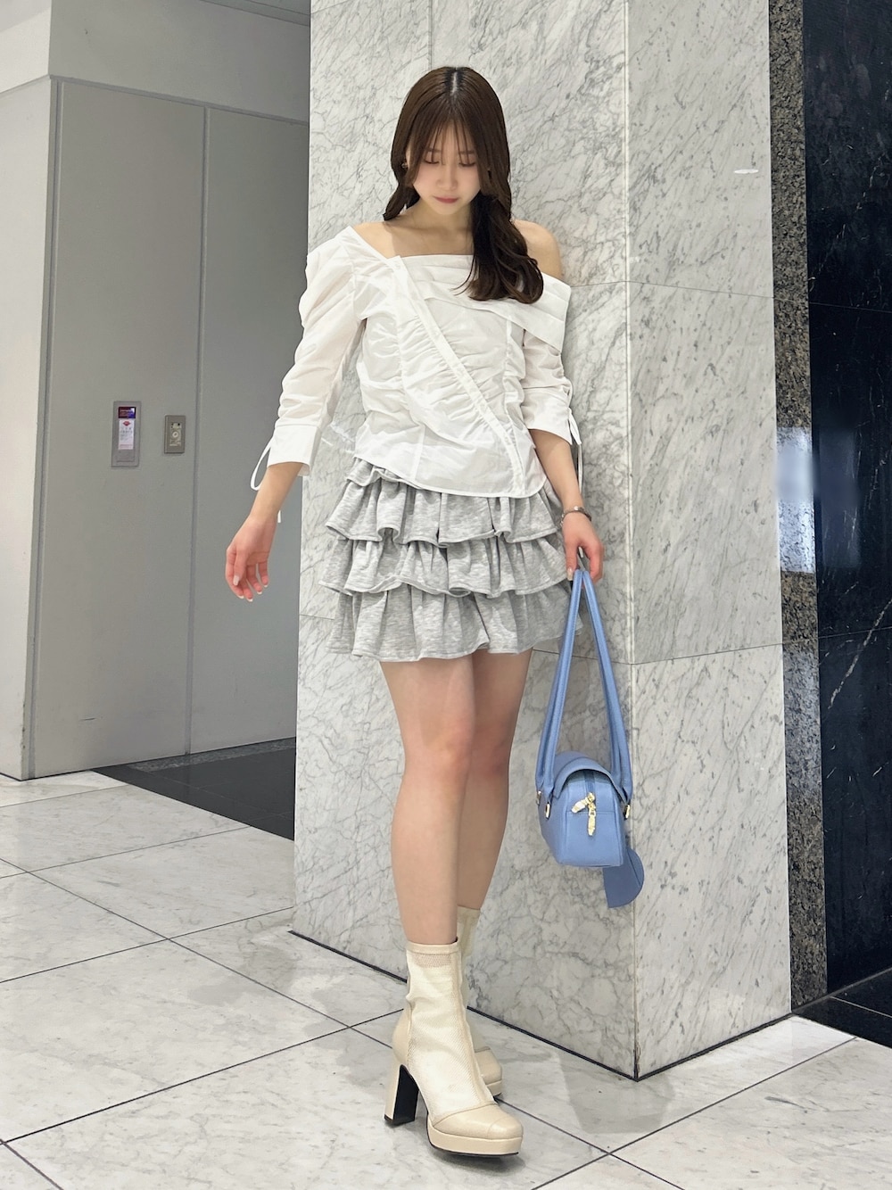 グレー系のスカート、ブルー系のハンドバッグ、ベージュ系のブーツを着用したレディースの春コーディネートの1枚目の写真