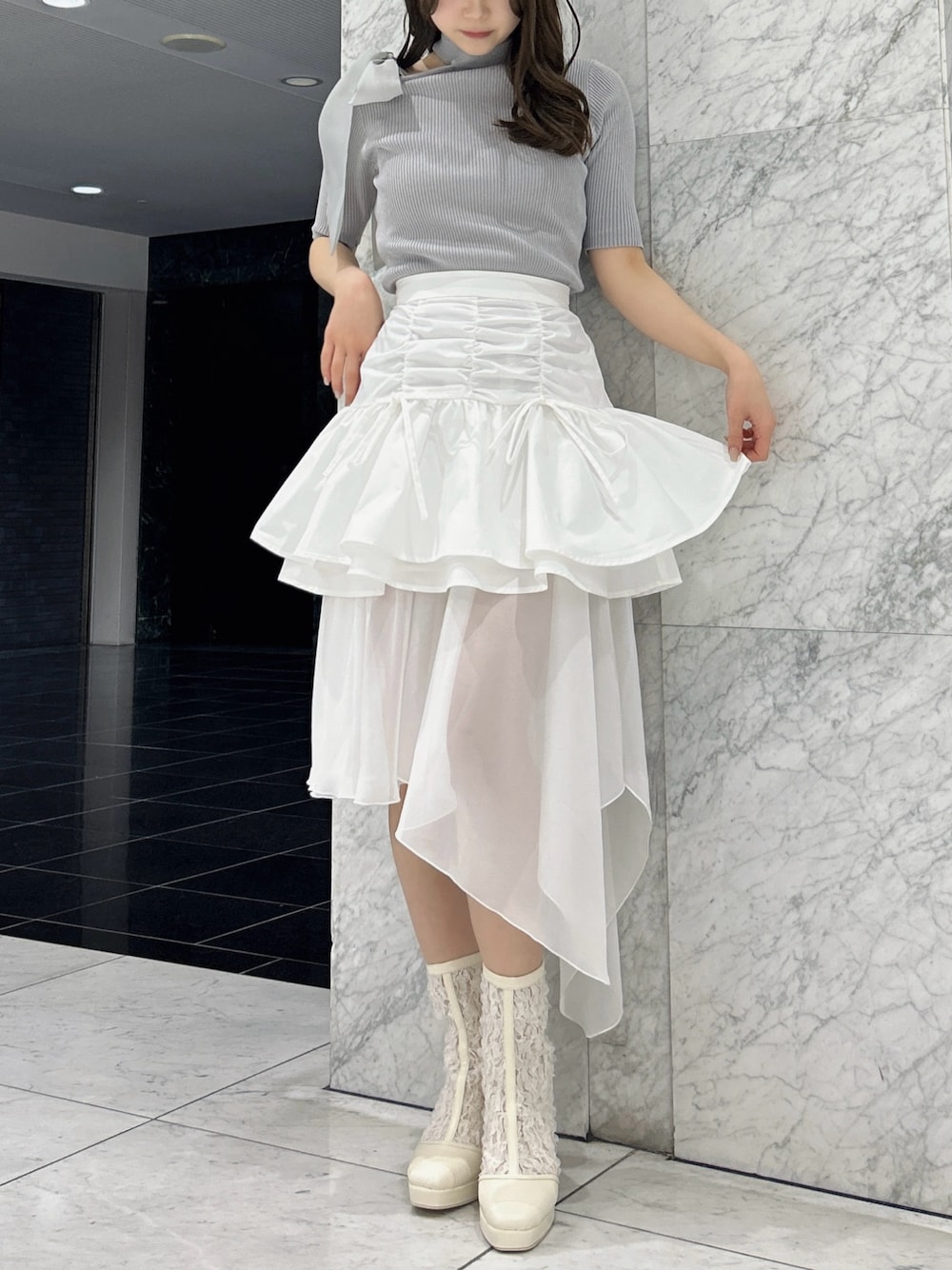グレー系のニット/セーター、ホワイト系のスカート、ホワイト系のブーツを着用したレディースの春コーディネートの1枚目の写真