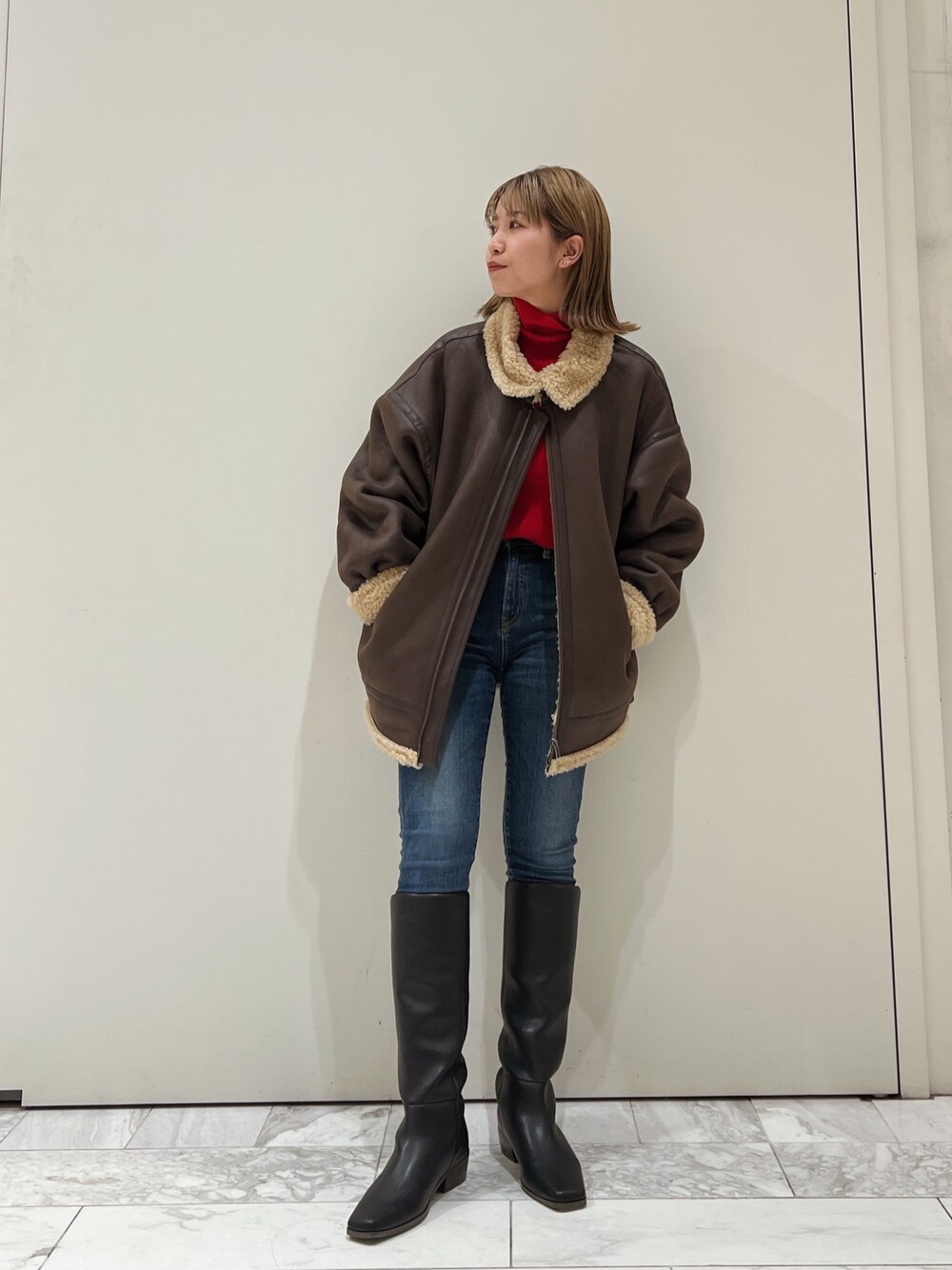 ブラウン系のムートンコート、レッド系のニット/セーター、ブルー系のデニムパンツを着用したレディースの冬コーディネートの1枚目の写真