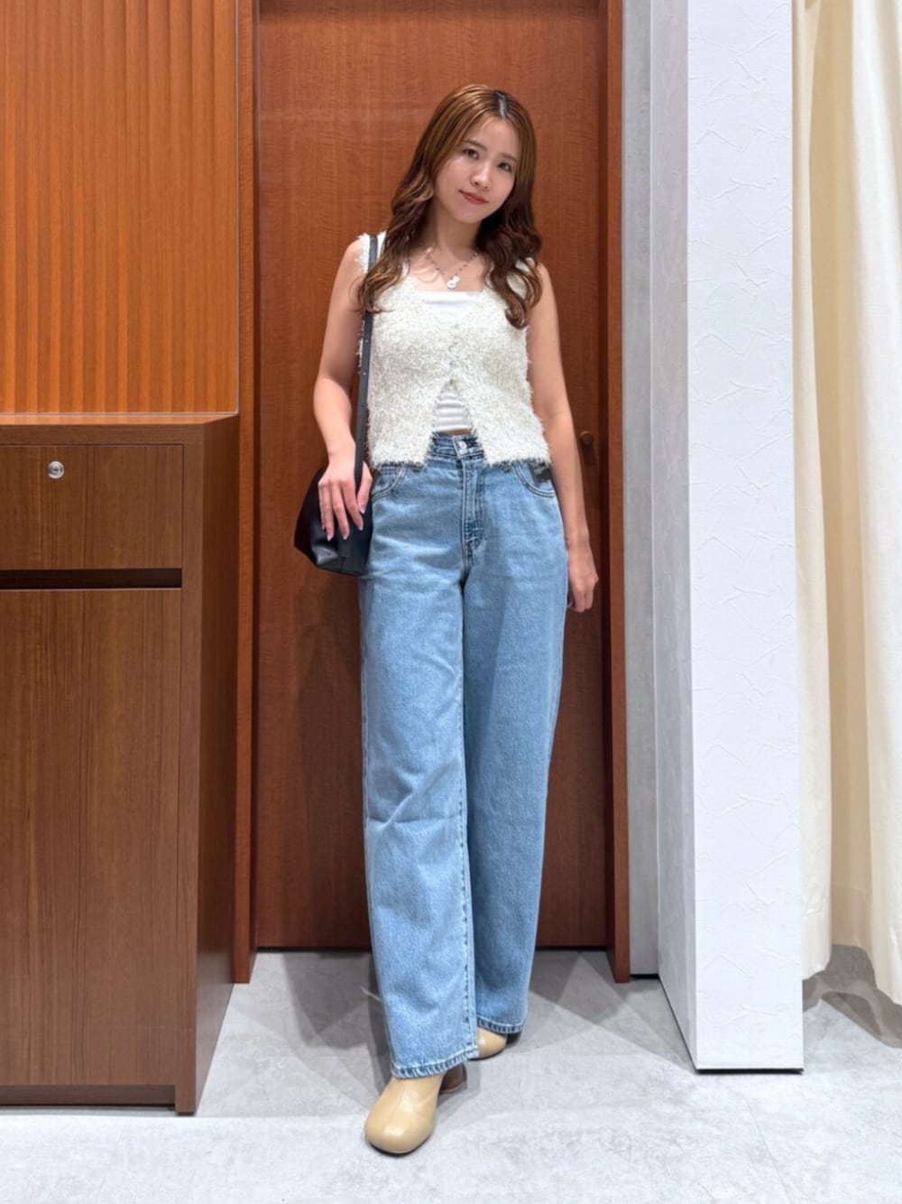 ブルー系のデニムパンツ、ホワイト系のベスト、ブラック系のハンドバッグを着用したレディースの夏コーディネートの1枚目の写真