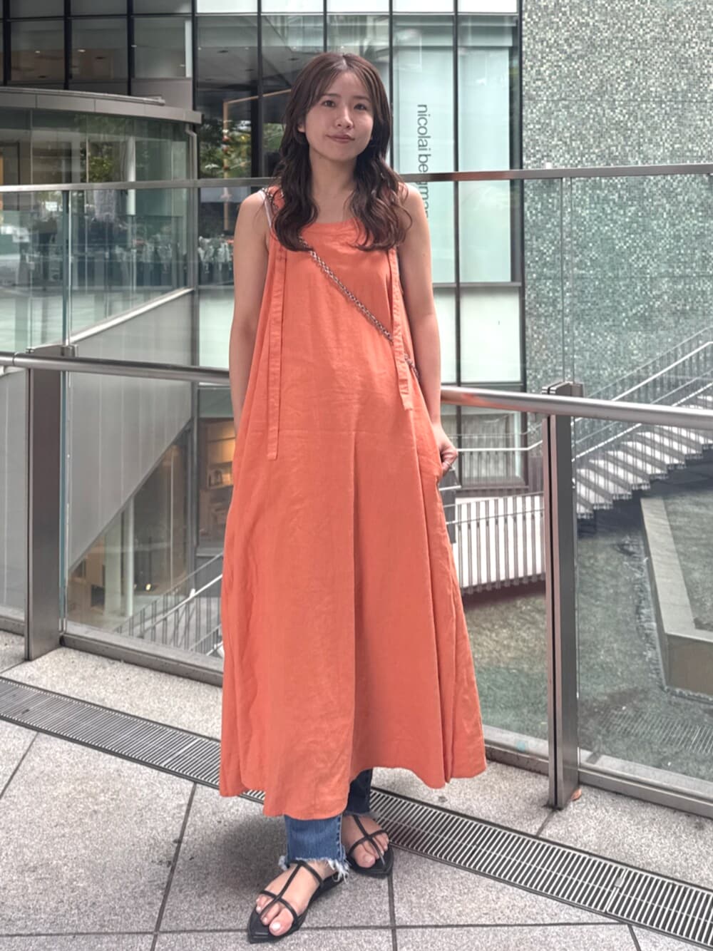 ブルー系のデニムパンツ、オレンジ系のワンピースを着用したレディースの春コーディネートの1枚目の写真