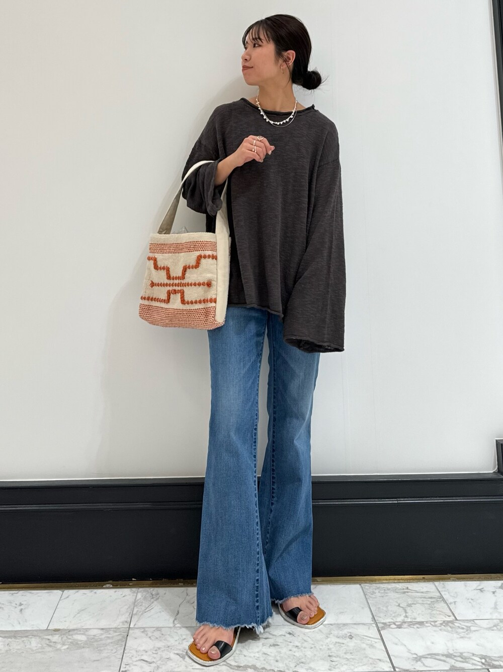 グレー系のニット/セーター、ブルー系のデニムパンツ、ブラック系のサンダルを着用したレディースの春コーディネートの1枚目の写真