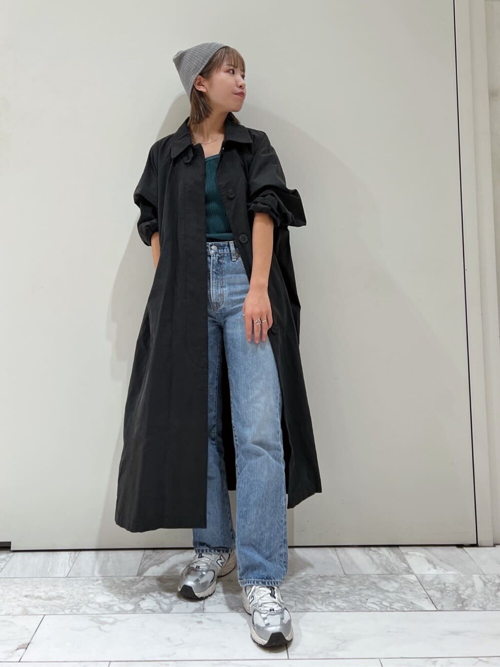 ブラック系のステンカラーコート、グリーン系のTシャツ/カットソー、ブルー系のデニムパンツを着用したレディースの秋コーディネートの1枚目の写真