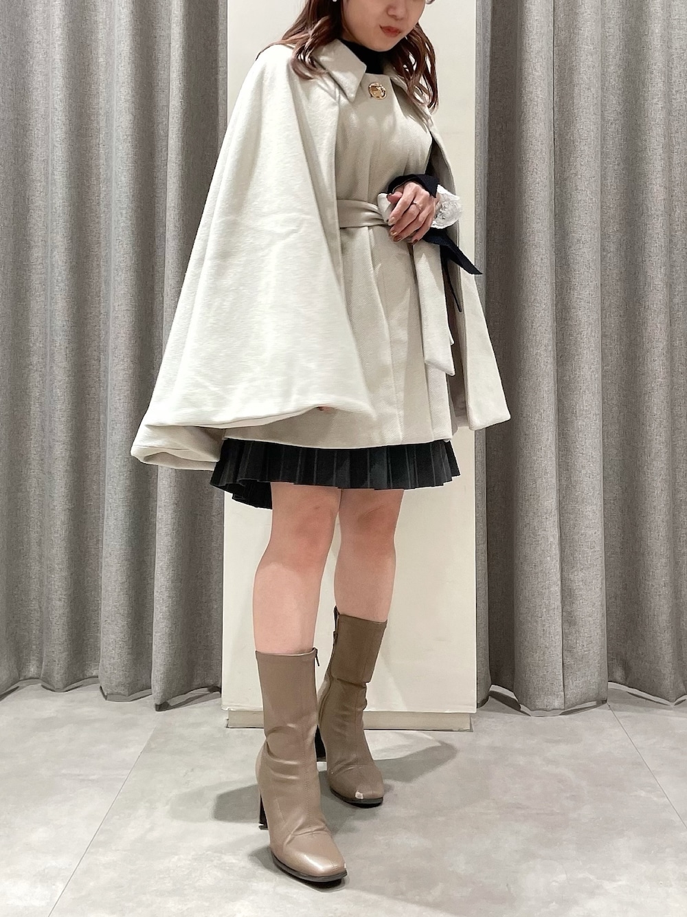 ホワイト系のポンチョ、ブラック系のニット/セーター、グレー系のスカートを着用したレディースの冬コーディネートの1枚目の写真