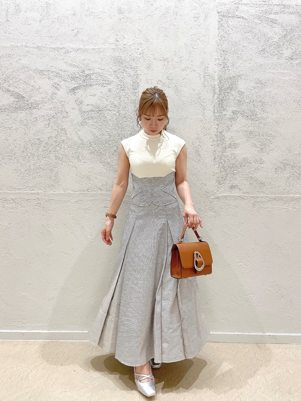 イエロー系のハンドバッグ、ホワイト系のワンピース、シルバー系のパンプスを着用したレディースの夏コーディネートの1枚目の写真