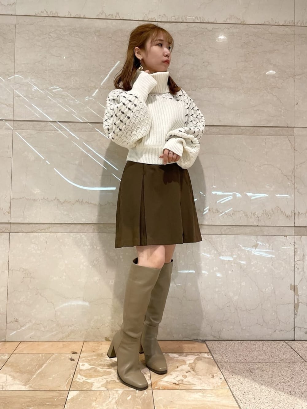 ブラウン系のスカート、ベージュ系のブーツ、ホワイト系のニット/セーターを着用したレディースの秋コーディネートの1枚目の写真