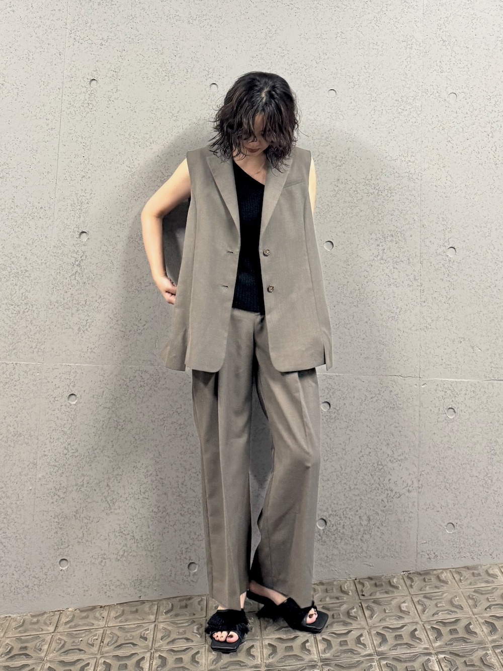 ベージュ系のベスト、ベージュ系のスラックス、ブラック系のサンダルを着用したレディースの夏コーディネートの1枚目の写真