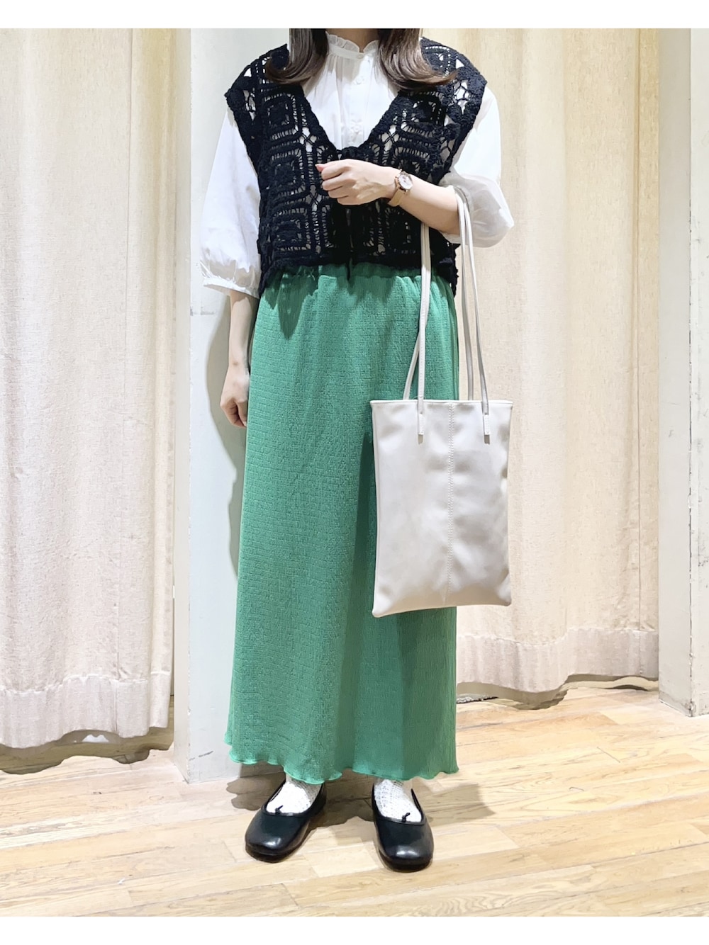 グリーン系のスカート、ホワイト系のトートバッグ、ブラック系のベストを着用したレディースの夏コーディネートの1枚目の写真