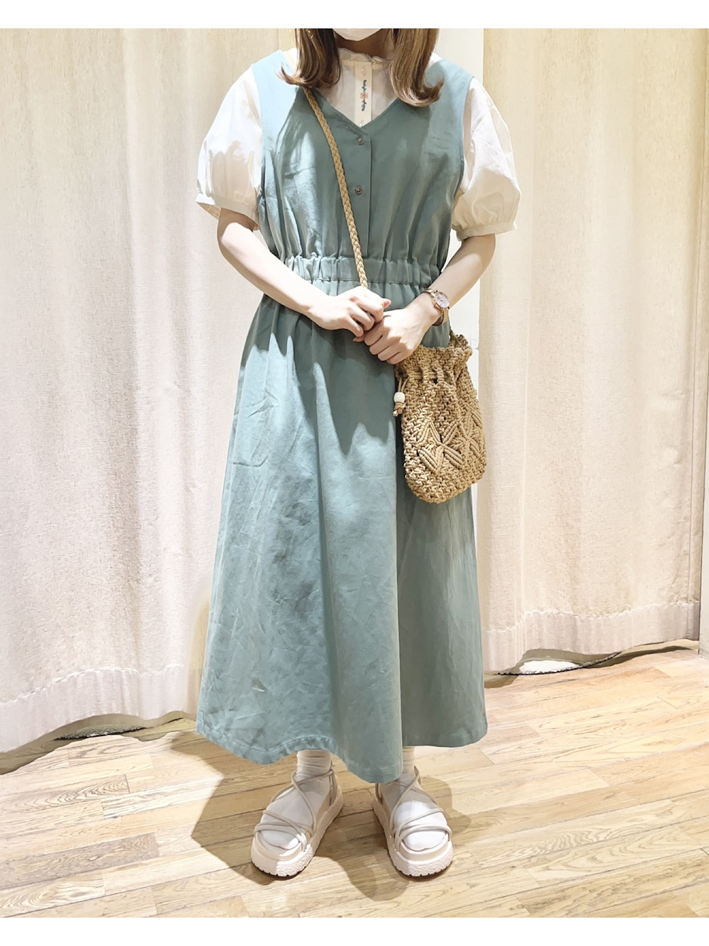 グリーン系のジャンパースカート、ホワイト系のサンダル、ベージュ系のショルダーバッグを着用したレディースの夏コーディネートの1枚目の写真