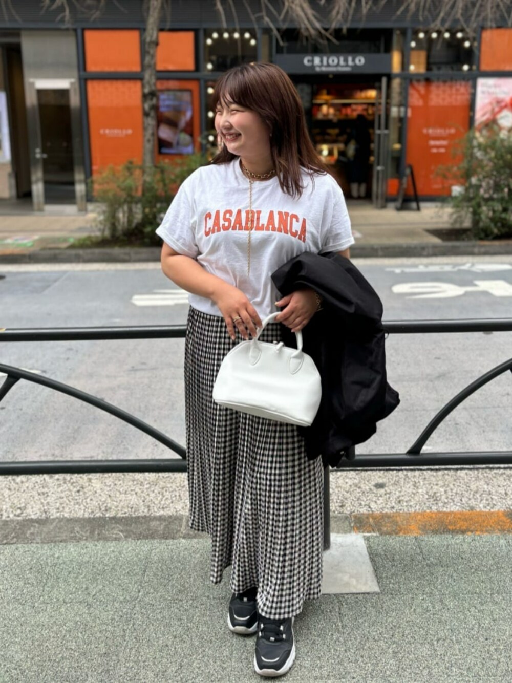 ブラック系のスカート、オレンジ系のTシャツ/カットソー、ホワイト系のボストンバッグを着用したレディースの春コーディネートの1枚目の写真