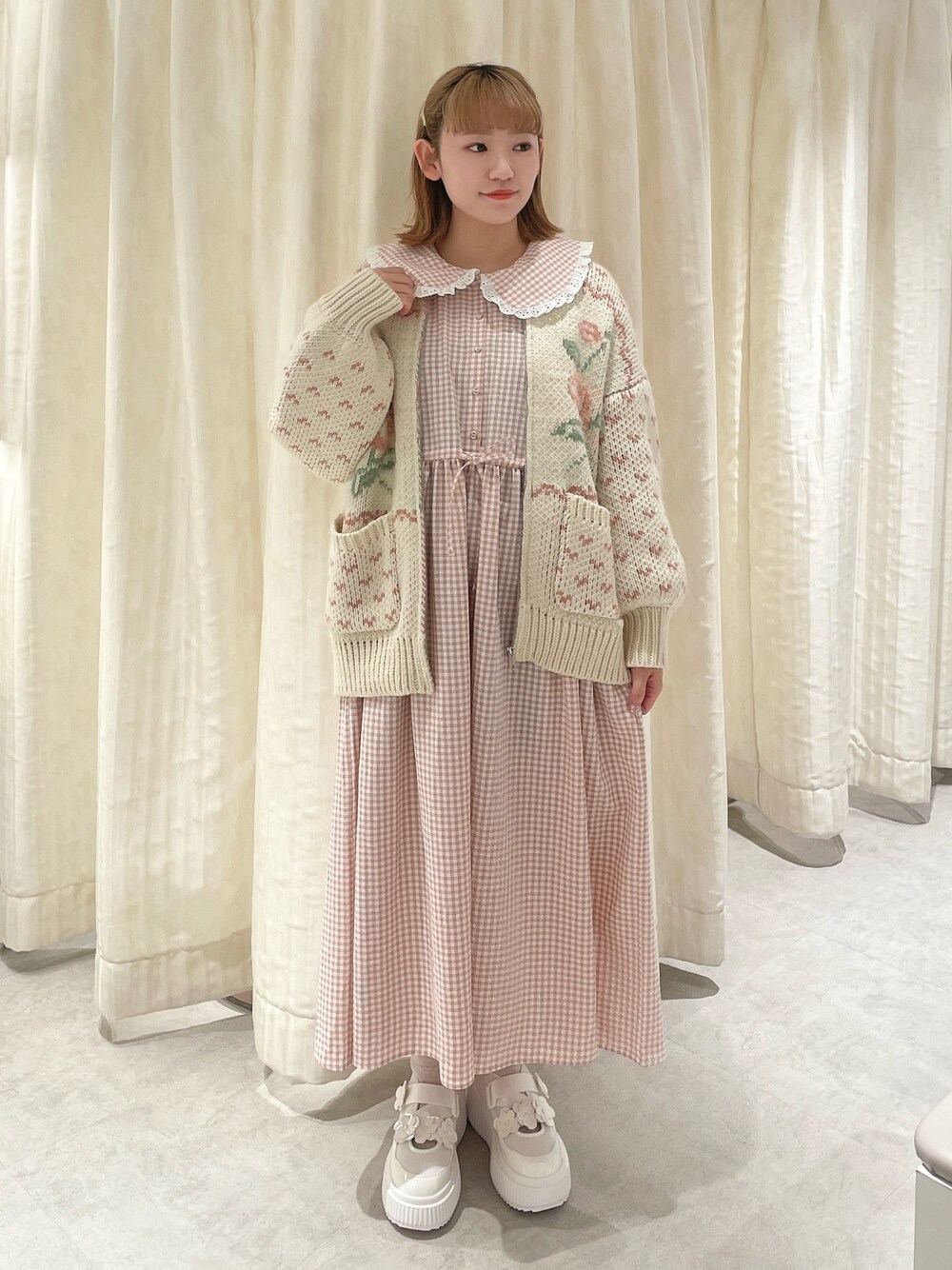 ピンク系のカーディガン/ボレロ、ピンク系のワンピース、ホワイト系のスニーカーを着用したレディースの冬コーディネートの1枚目の写真