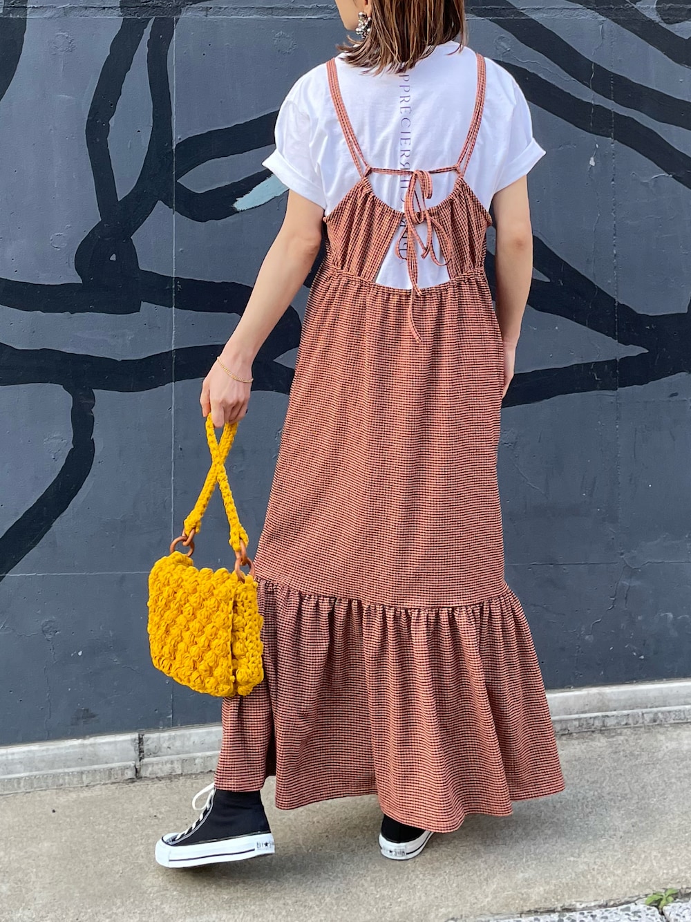 オレンジ系のワンピース、ホワイト系のTシャツ/カットソー、ブラック系のスニーカーを着用したレディースの春コーディネートの1枚目の写真