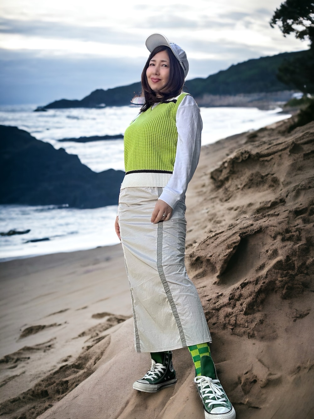 グリーン系のベスト、グレー系のスカート、ホワイト系のチュニックを着用したレディースの春コーディネートの1枚目の写真