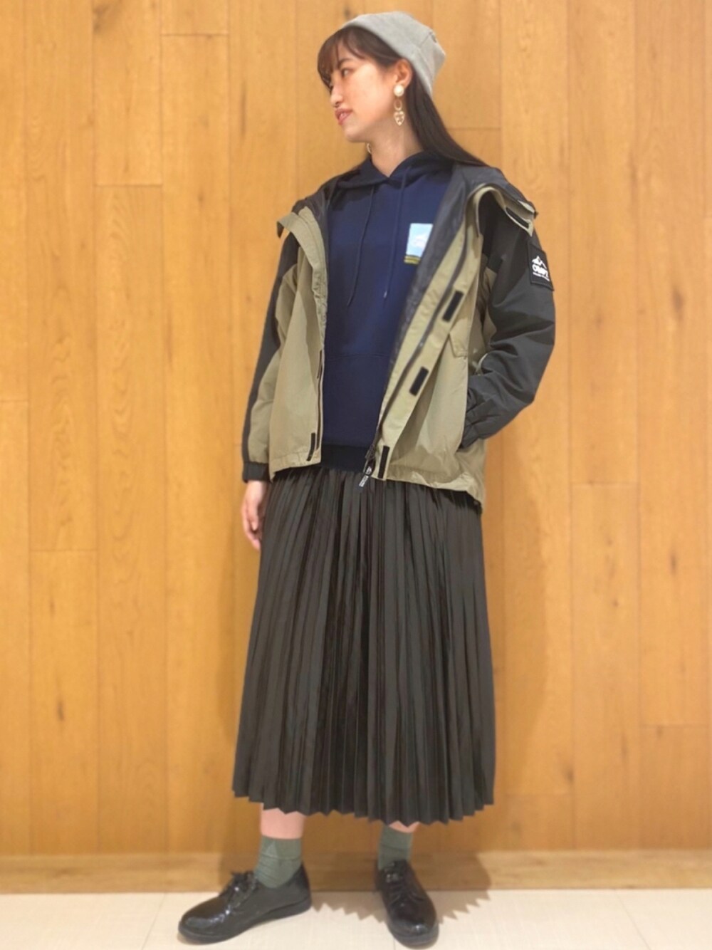 ブラック系のスカート、グリーン系のマウンテンパーカー、ブルー系のパーカーを着用したレディースの秋コーディネートの1枚目の写真