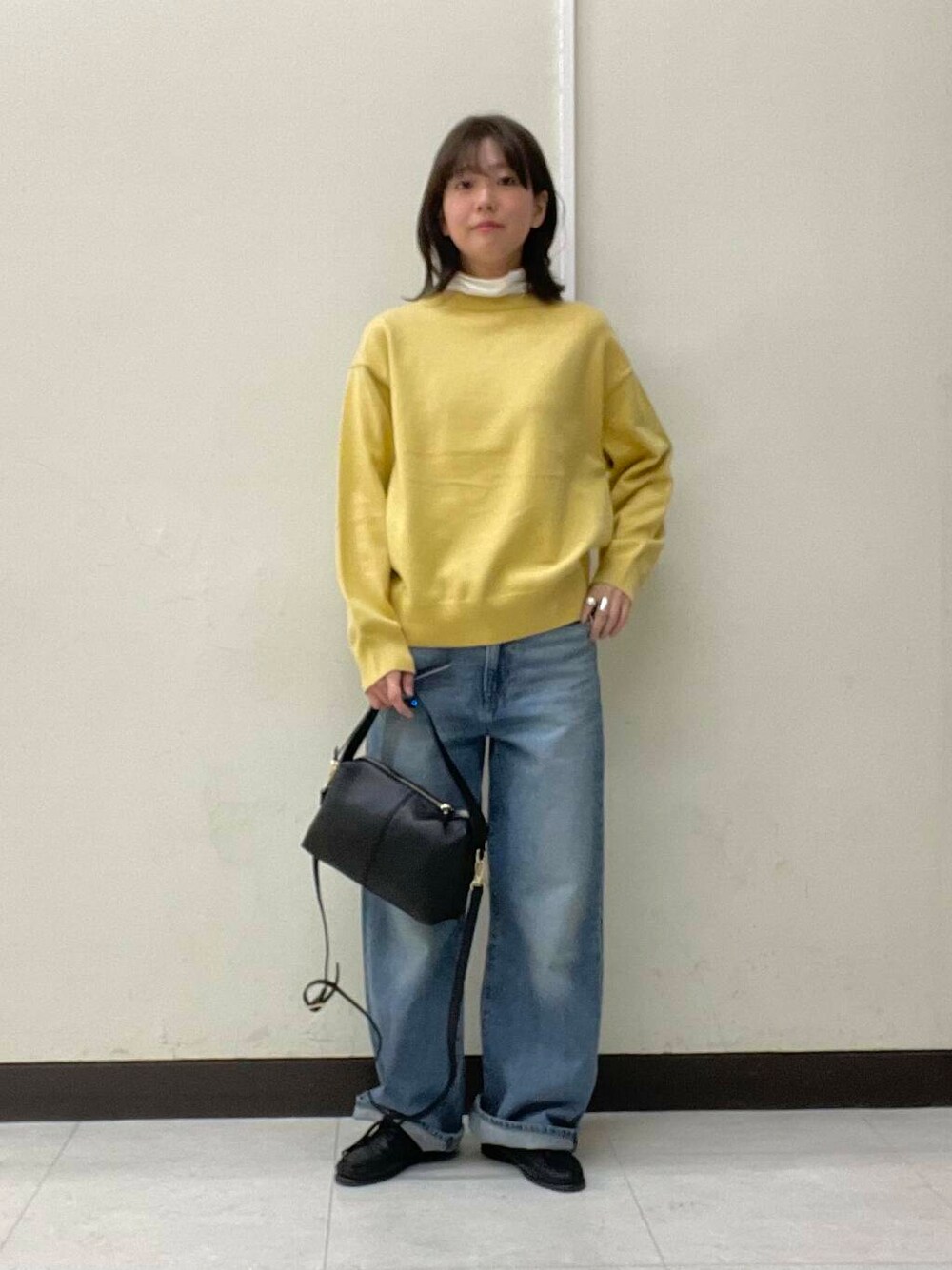 イエロー系のニット/セーター、ブルー系のデニムパンツ、ブラック系のショルダーバッグを着用したレディースの冬コーディネートの1枚目の写真