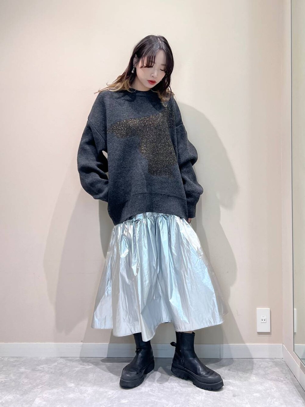 シルバー系のスカート、グレー系のニット/セーター、シルバー系のピアス(両耳用)を着用したレディースの冬コーディネートの1枚目の写真