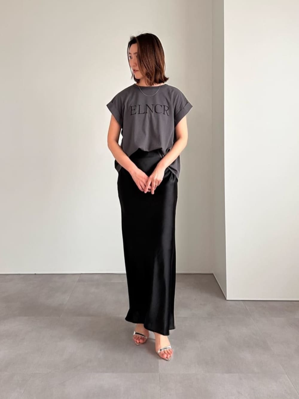 ブラック系のスカート、シルバー系のサンダル、グレー系のTシャツ/カットソーを着用したレディースの春コーディネートの1枚目の写真