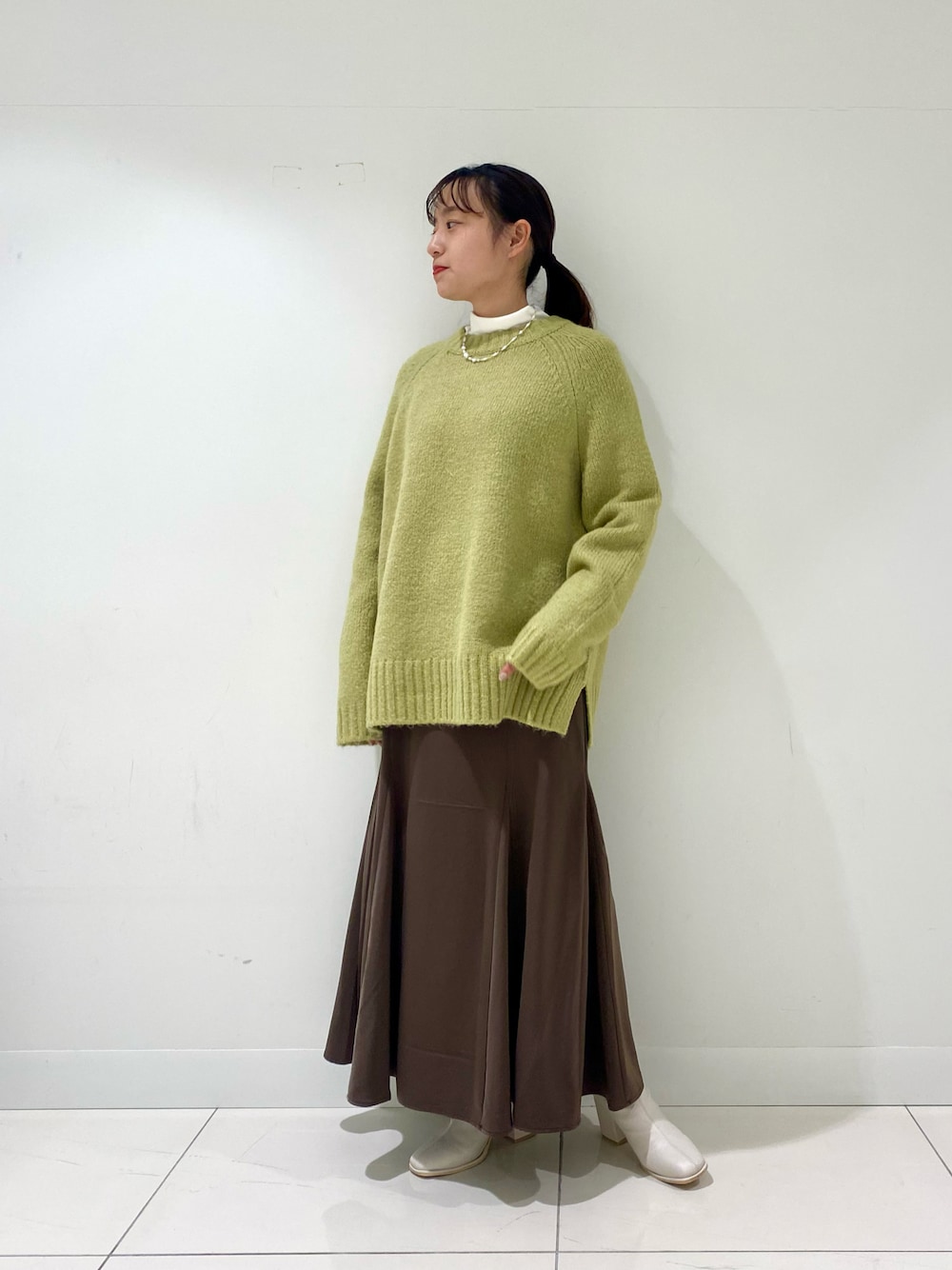 グリーン系のニット/セーター、ブラウン系のスカート、ホワイト系のブーツを着用したレディースの冬コーディネートの1枚目の写真