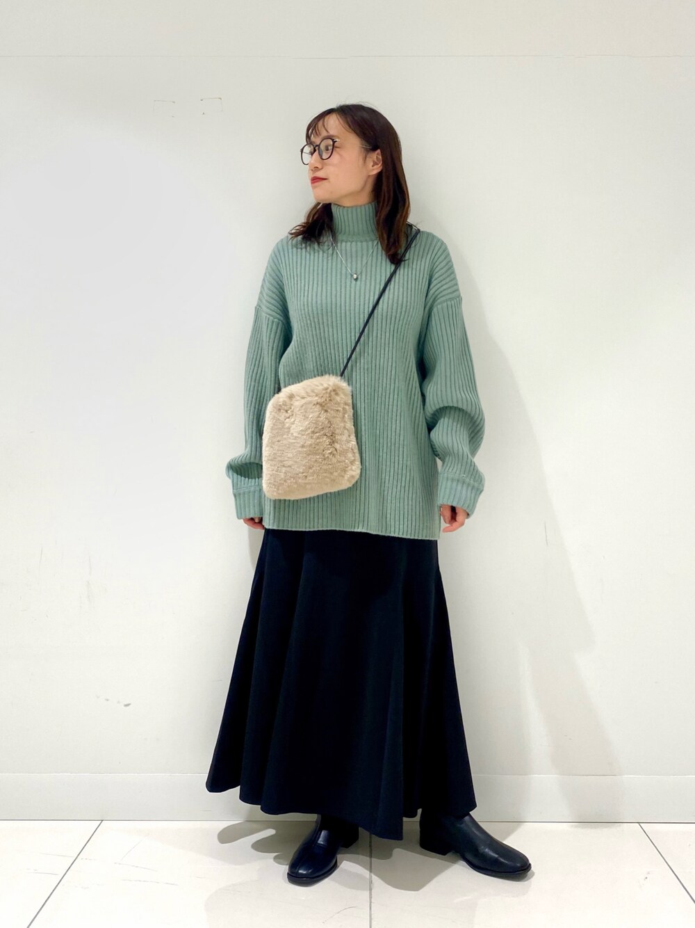 グリーン系のニット/セーター、ブラック系のスカート、ベージュ系のショルダーバッグを着用したレディースの冬コーディネートの1枚目の写真