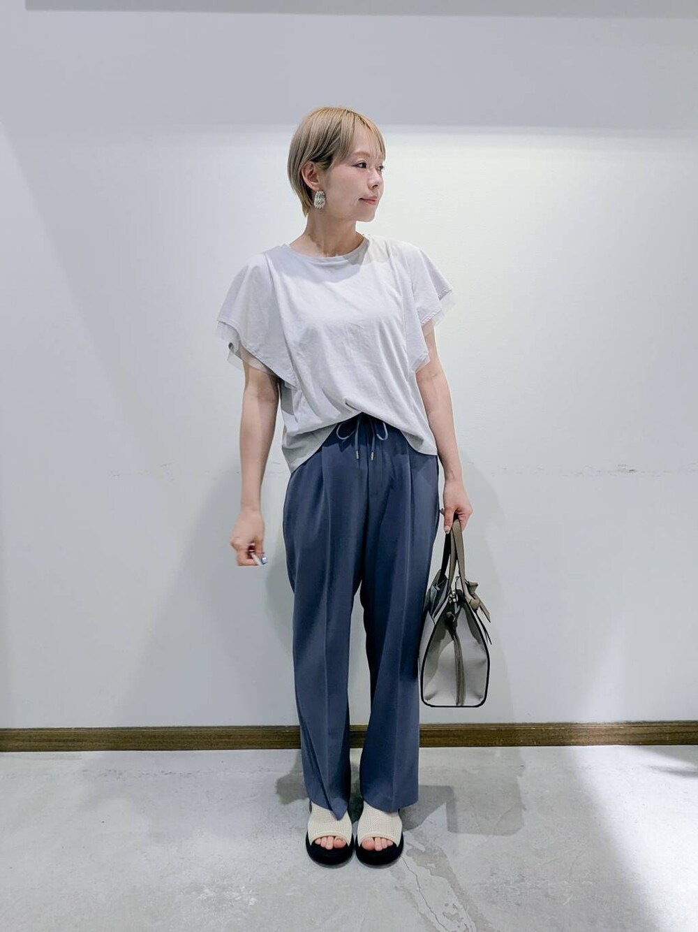 ホワイト系のショルダーバッグ、グレー系のTシャツ/カットソー、ブルー系のスラックスを着用したレディースの秋コーディネートの1枚目の写真