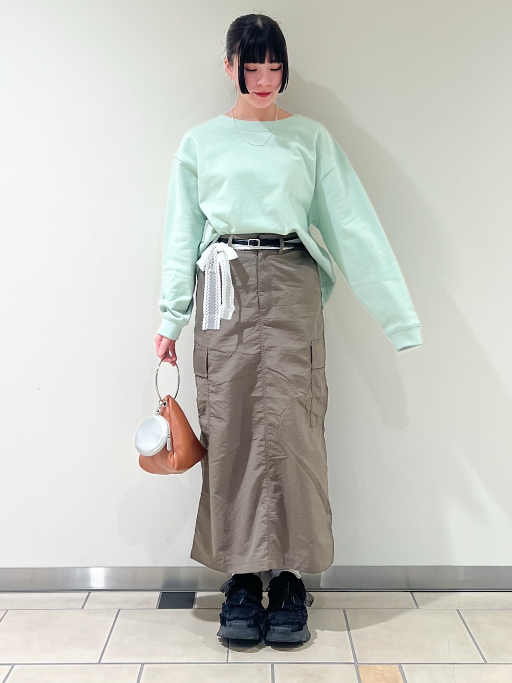 イエロー系のハンドバッグ、グリーン系のスウェット、ホワイト系のネックレスを着用したレディースの春コーディネートの1枚目の写真