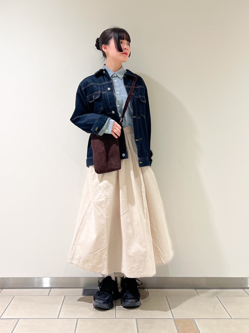 ホワイト系のスカート、ブルー系のデニムジャケット、ブラウン系のショルダーバッグを着用したレディースの秋コーディネートの1枚目の写真