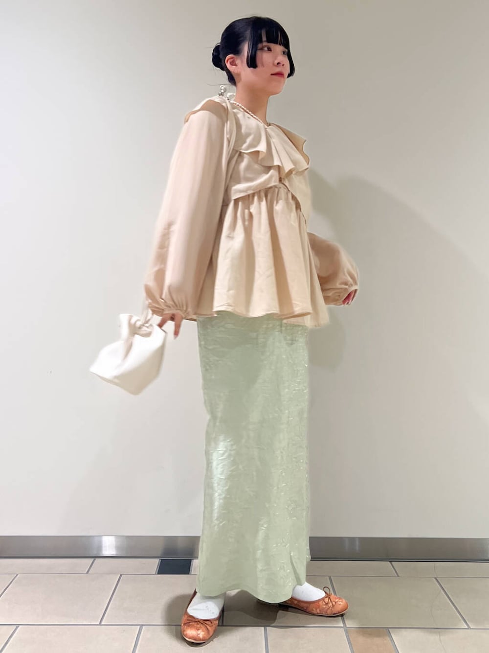 イエロー系のパンプス、グリーン系のスカート、ホワイト系のショルダーバッグを着用したレディースの春コーディネートの1枚目の写真