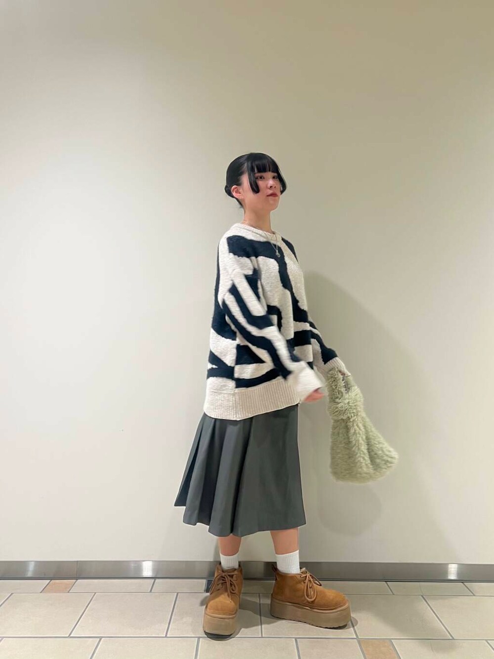 グレー系のスカート、グリーン系のハンドバッグ、ホワイト系のニット/セーターを着用したレディースの冬コーディネートの1枚目の写真