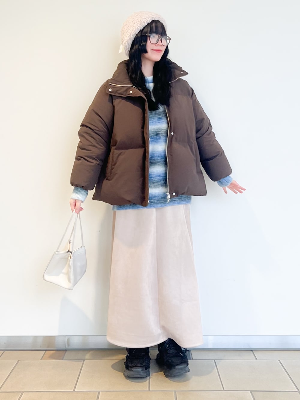 ベージュ系のスカート、ブルー系のニット/セーター、ブラウン系のダウンジャケット/コートを着用したレディースの冬コーディネートの1枚目の写真