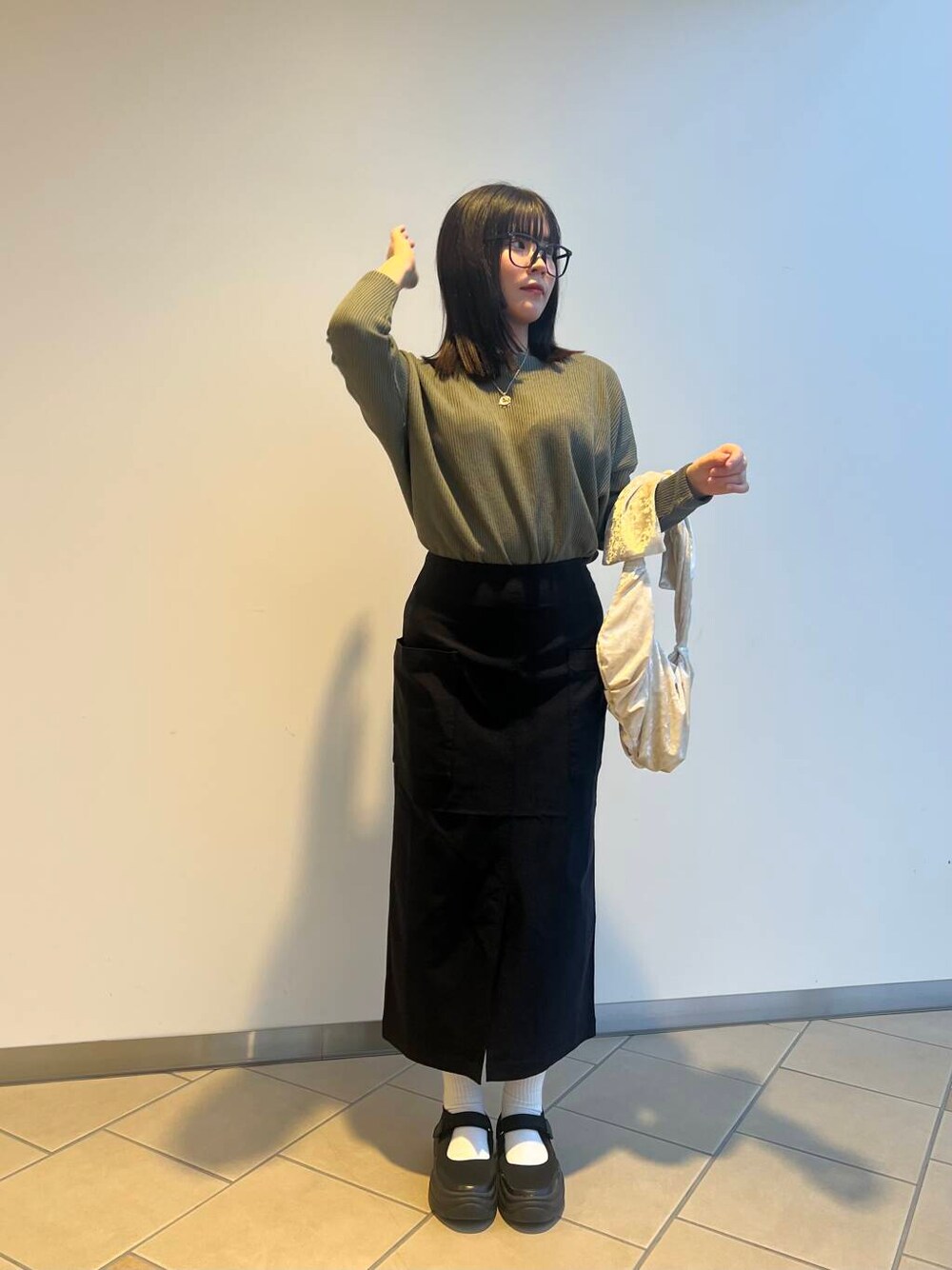 ベージュ系のハンドバッグ、ブラック系のスカート、グリーン系のニット/セーターを着用したレディースの夏コーディネートの1枚目の写真