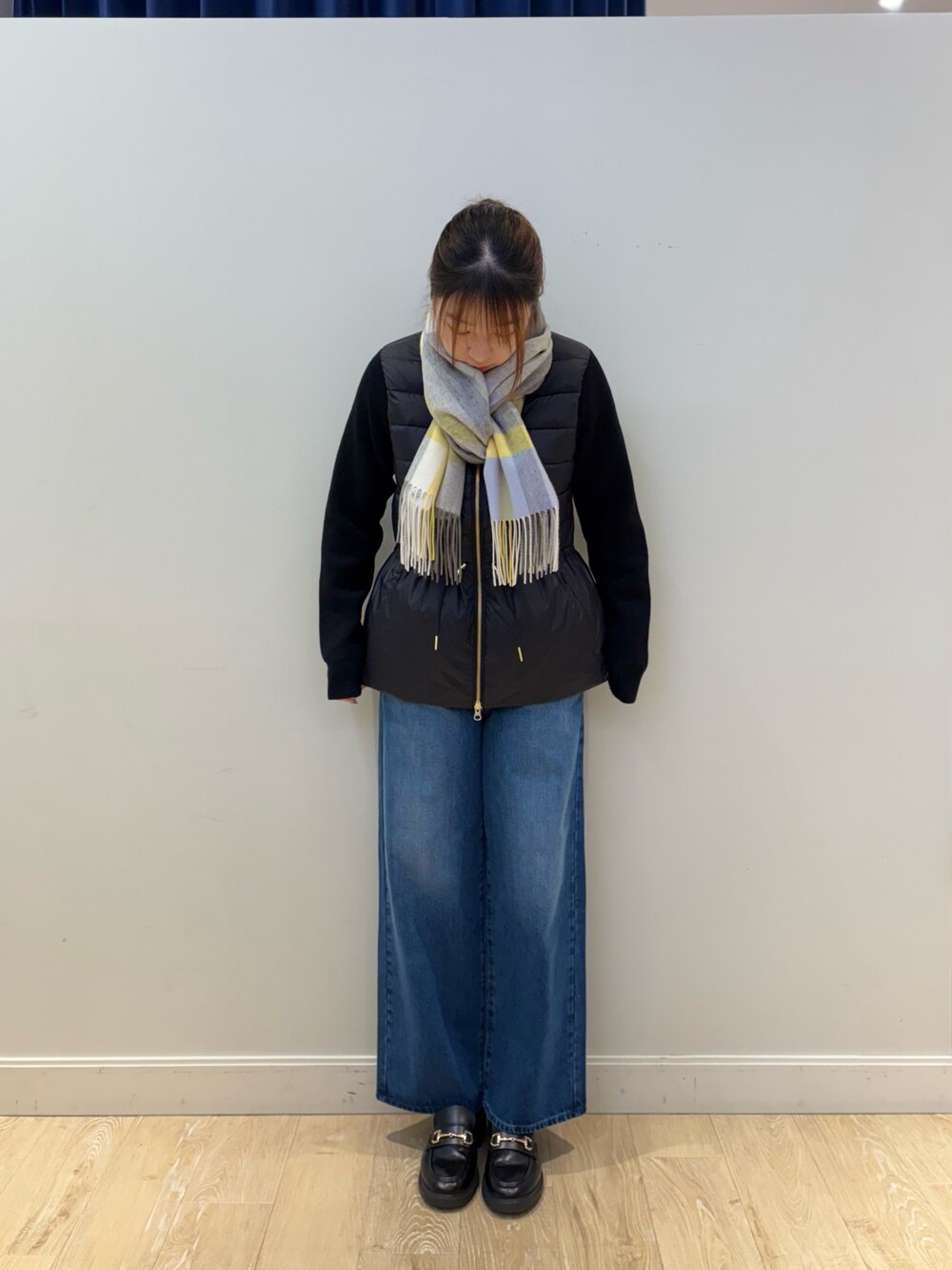 ブルー系のデニムパンツ、ブラック系のダウンジャケット/コート、ホワイト系のストール/ショールを着用したレディースの秋コーディネートの1枚目の写真