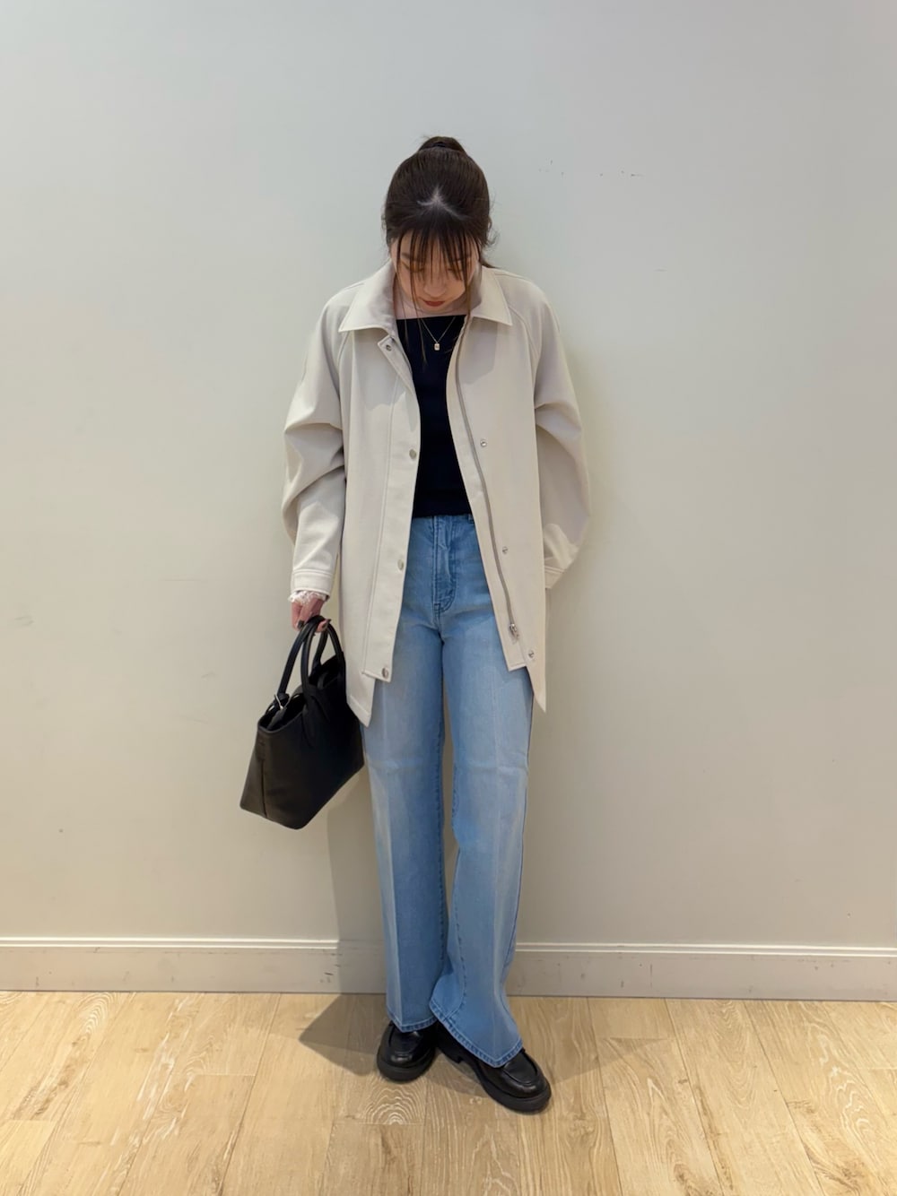 ブルー系のデニムパンツ、ブラック系のトートバッグ、ベージュ系のステンカラーコートを着用したレディースの冬コーディネートの1枚目の写真