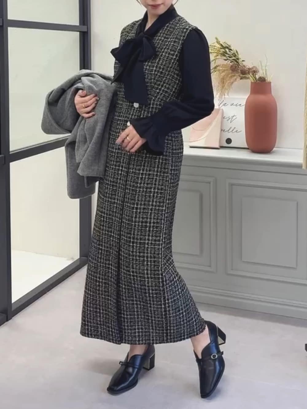 ブラック系のシャツ/ブラウス、ブラック系のジャンパースカート、グレー系のチェスターコートを着用したレディースの冬コーディネートの1枚目の写真