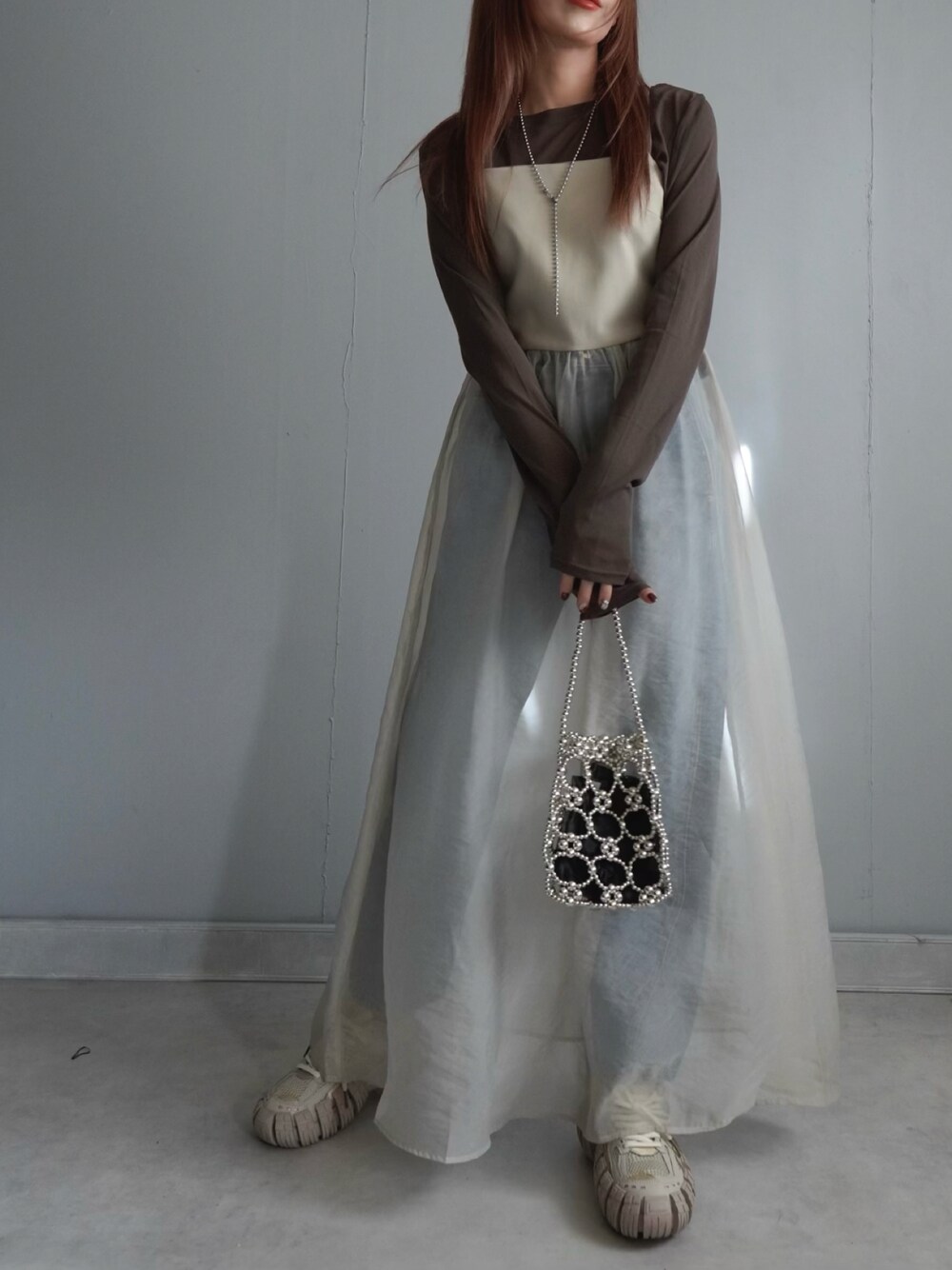 ベージュ系のワンピース、ブルー系のデニムパンツ、ブラウン系のトップスを着用したレディースの春コーディネートの1枚目の写真