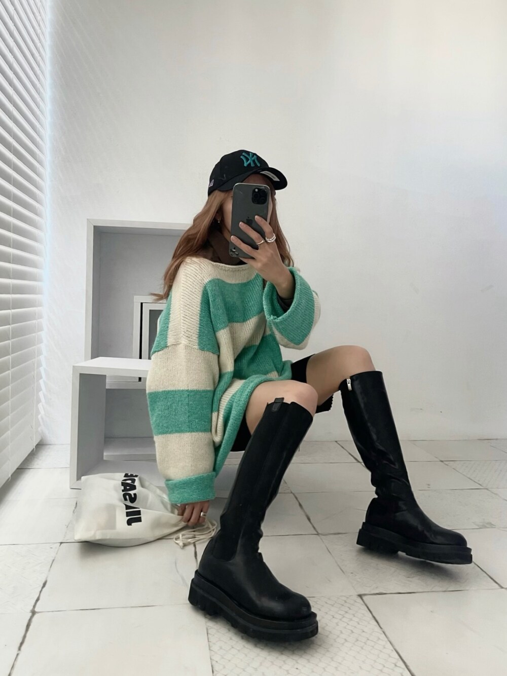 グリーン系のニット/セーター、ブラック系のブーツ、ホワイト系のショルダーバッグを着用したレディースの秋コーディネートの1枚目の写真
