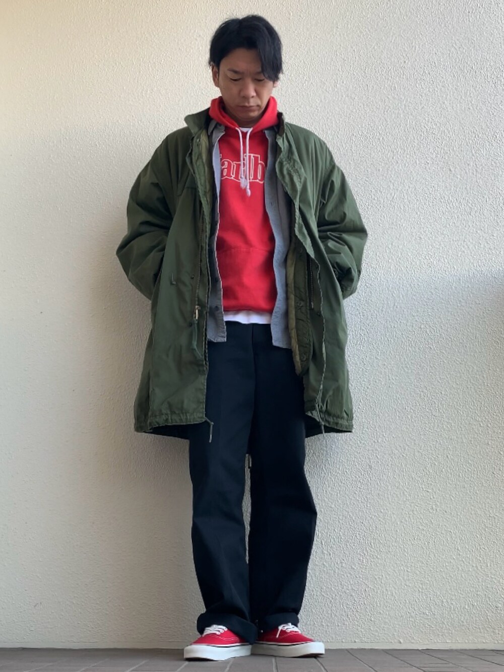 グリーン系のモッズコート、ブラック系のチノパンツ、レッド系のスニーカーを着用したメンズの冬コーディネートの1枚目の写真
