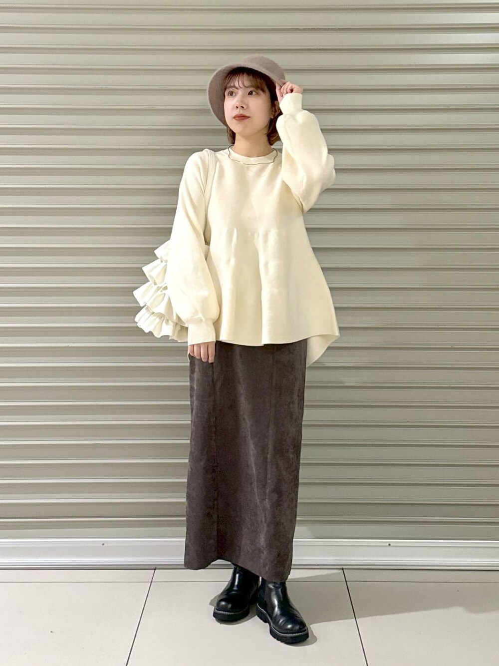 ブラウン系のスカート、ブラック系のブーツ、ホワイト系のトートバッグを着用したレディースの冬コーディネートの1枚目の写真