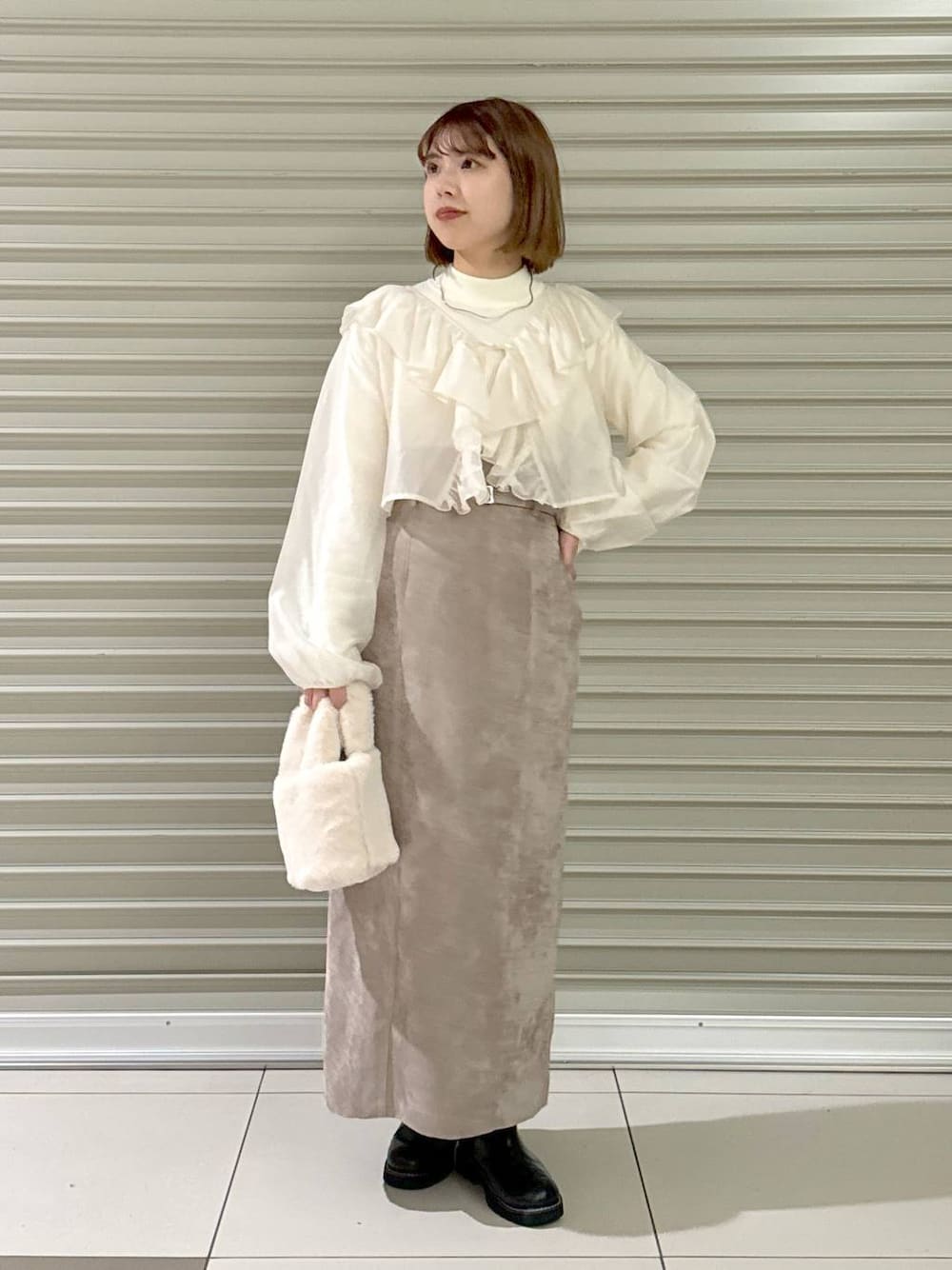 ブラウン系のスカート、ブラック系のブーツ、ホワイト系のハンドバッグを着用したレディースの冬コーディネートの1枚目の写真