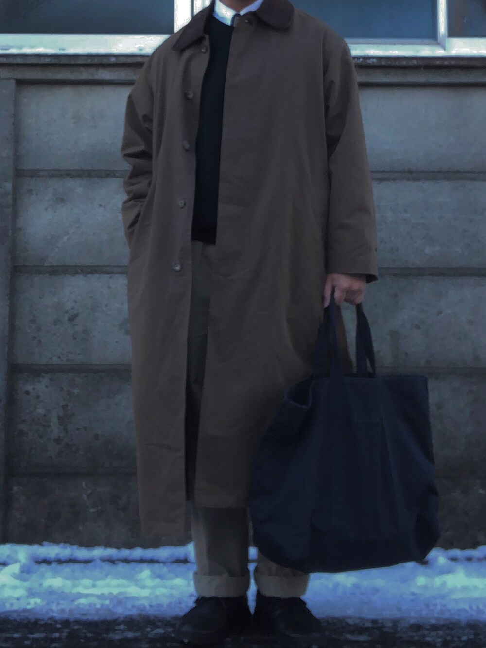 ブルー系のトートバッグ、ベージュ系のチノパンツ、ブラック系のドレスシューズを着用したメンズの冬コーディネートの1枚目の写真